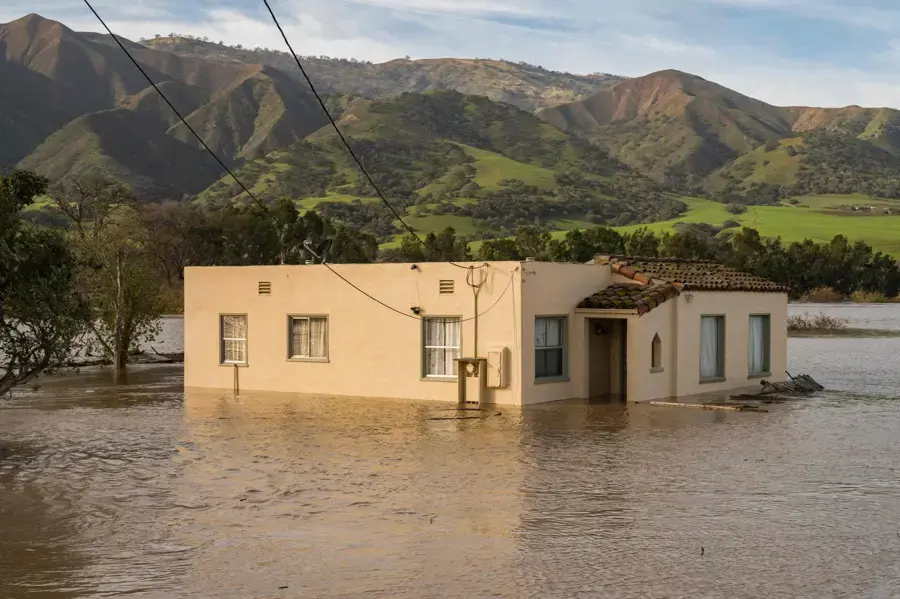 Floodwater around a single-story home below green California foothills