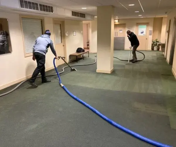 Two technicians extracting water from carpet in an office lobby