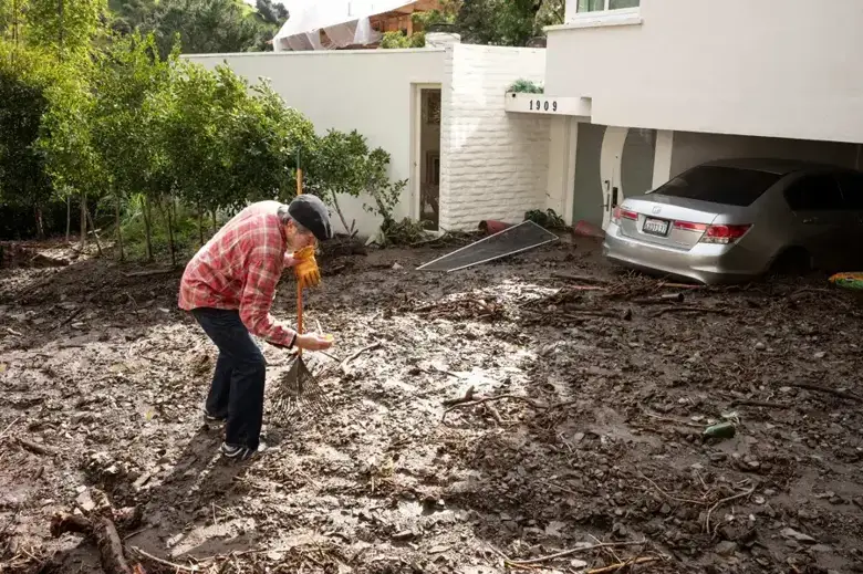 Homeowner clearing storm mud washed down against a house and garage
